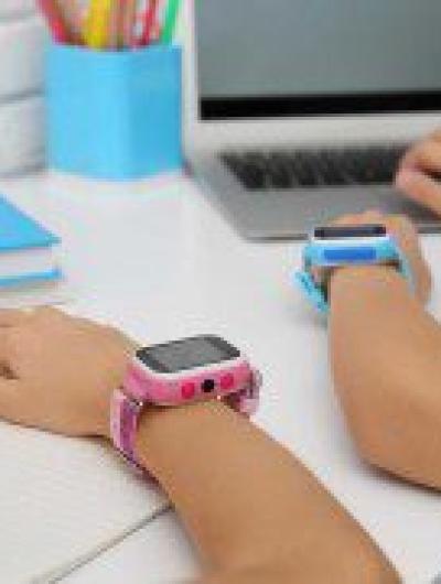 Children with stylish smart watches at white table, closeup